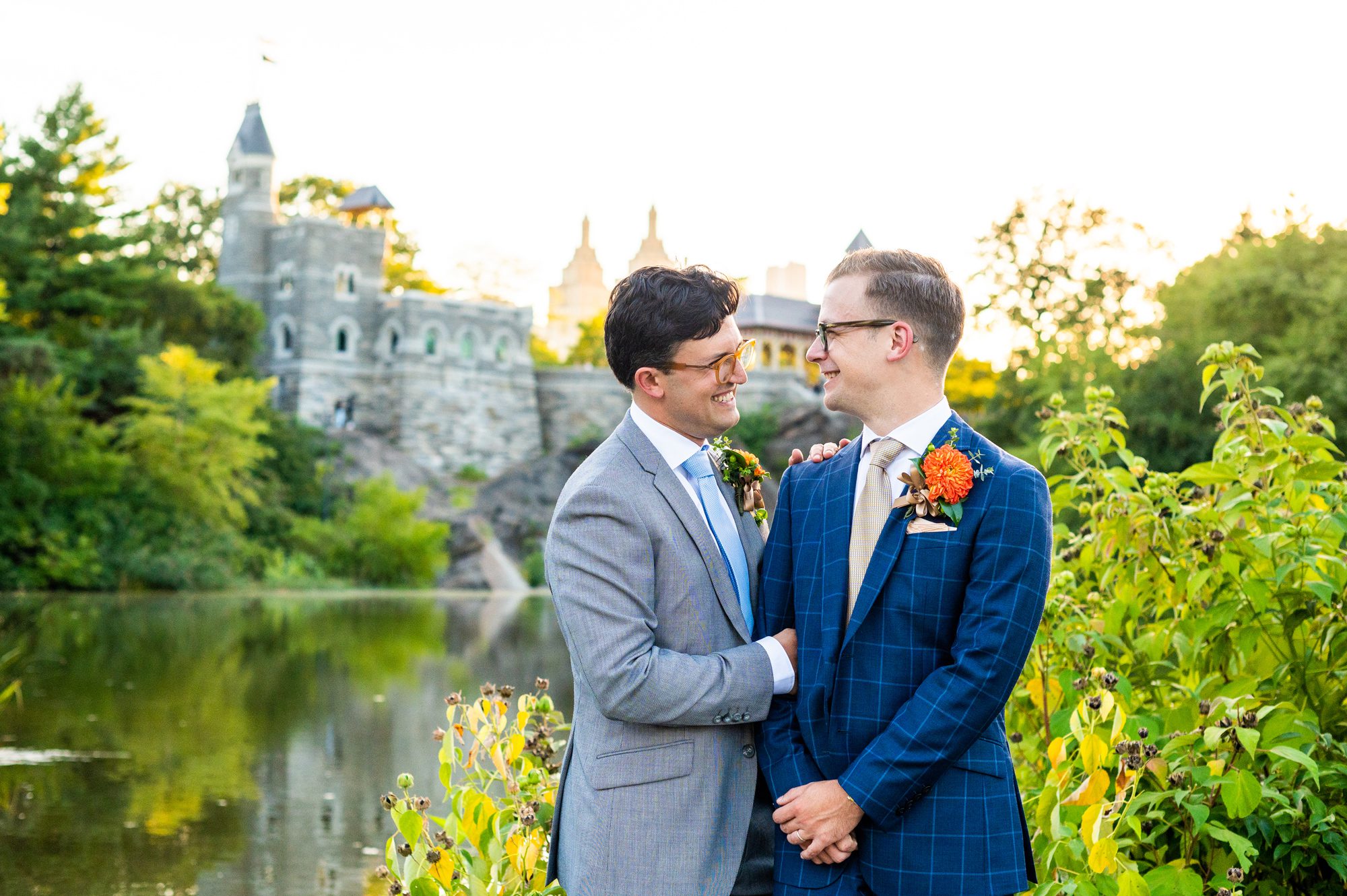Two grooms look at each other after their NYC Elopement. They are standing in front of the Belvedere Castle in Central Park at sunset.  