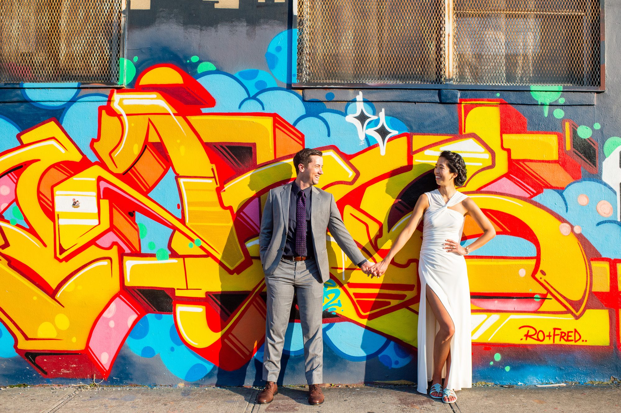 A couple poses in front of bright yellow street art after their wedding in Bushwick, Brooklyn. 