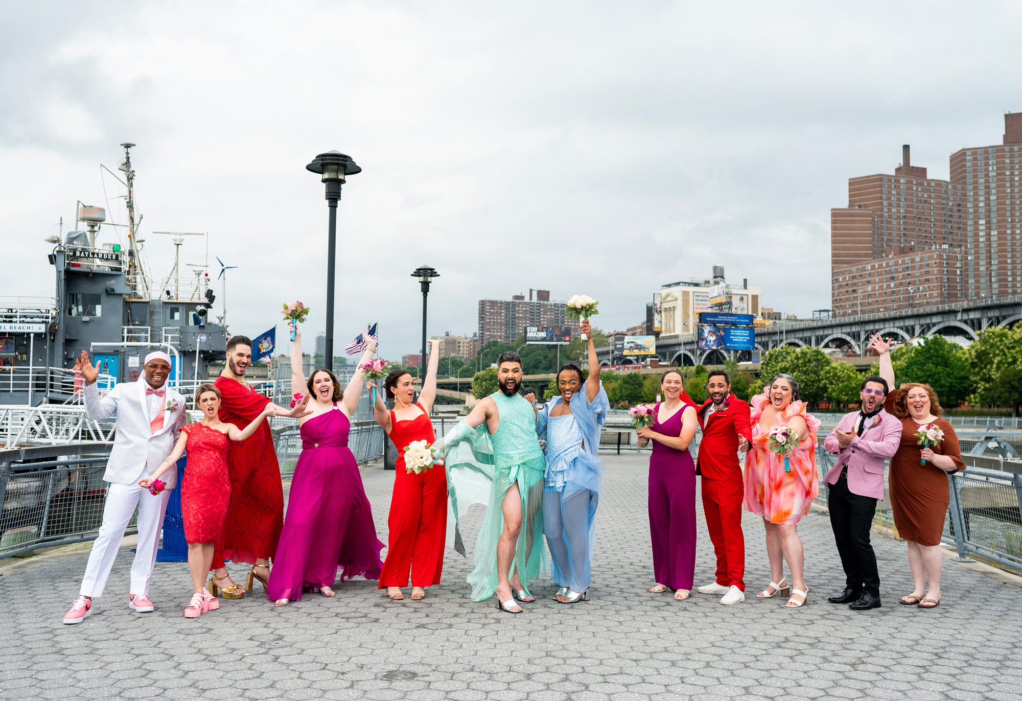 A queer wedding couple in NYC with their wedding party in very colorful outfits cheering before their New York wedding at Baylander Steel Beach. 
