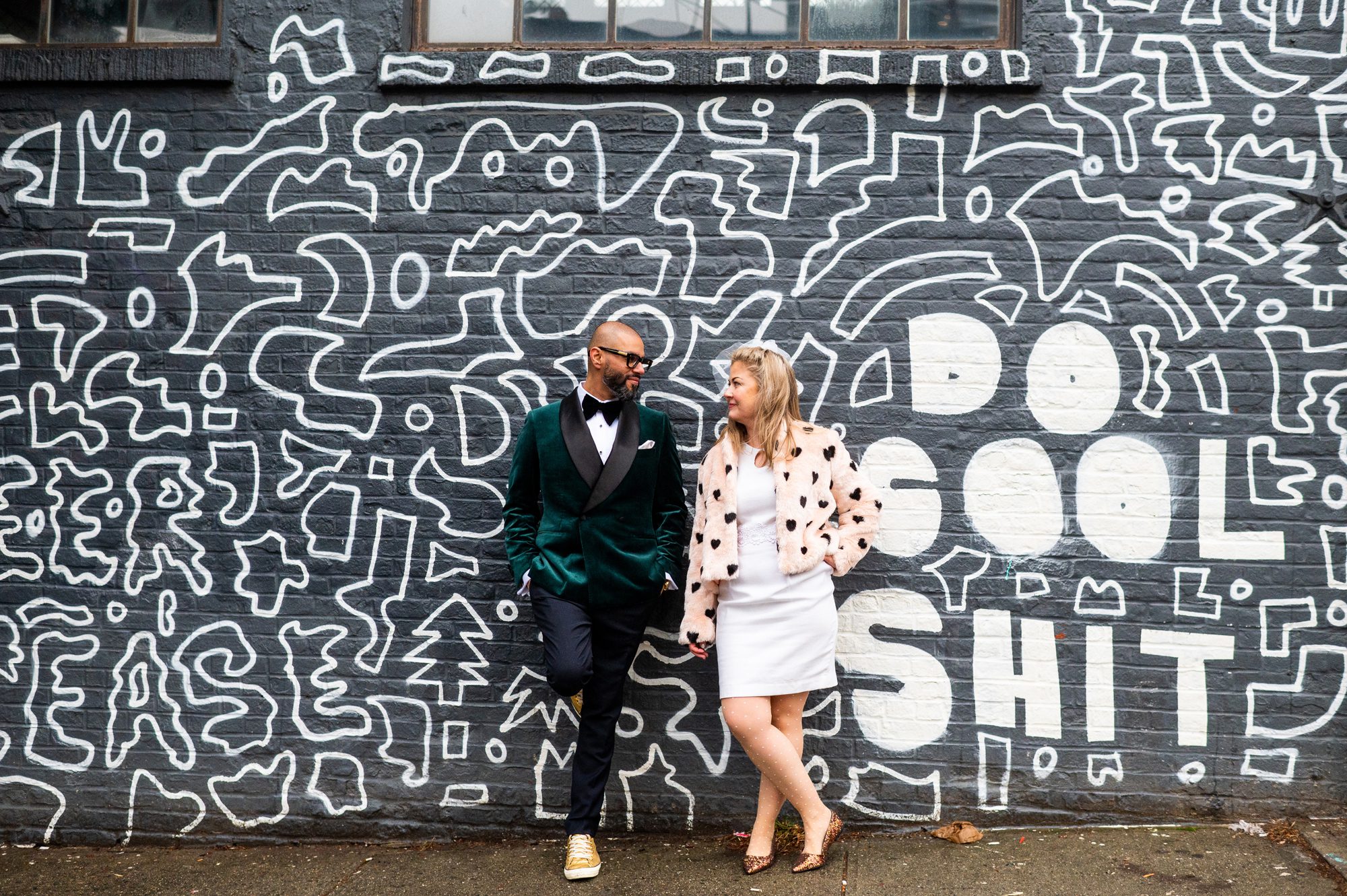 Bride and Groom in front of a street art mural that says Do Cool Shit. 