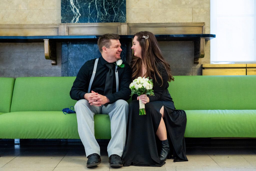 A couple waiting to get married at NYC City Hall sits on a green couch. 