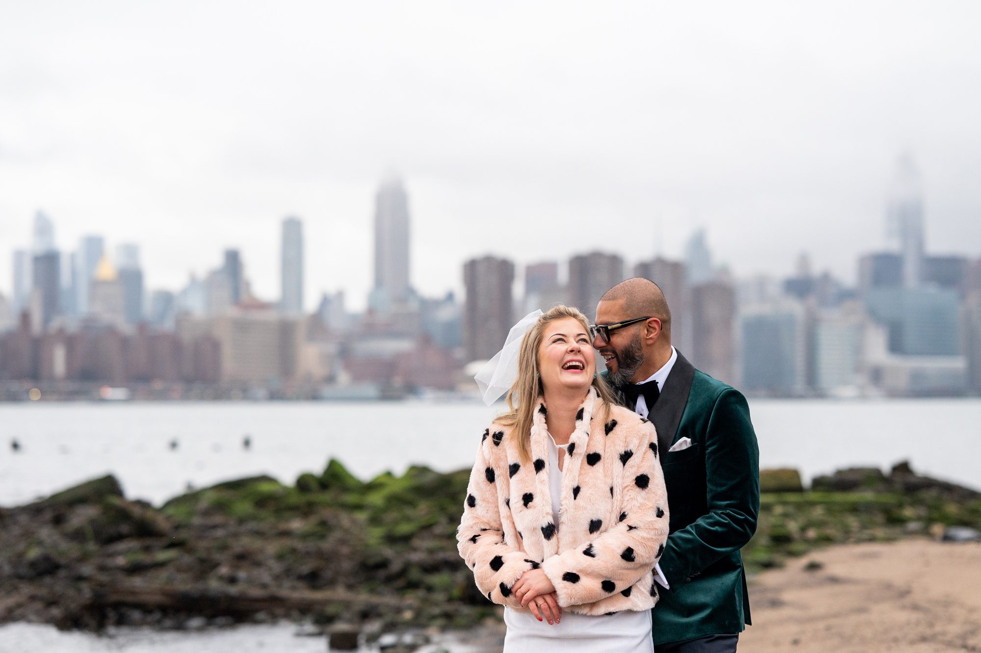 Couple snuggling on the waterfront with the NYC skyline behind them in Williamsburg after their NYC Elopement. 