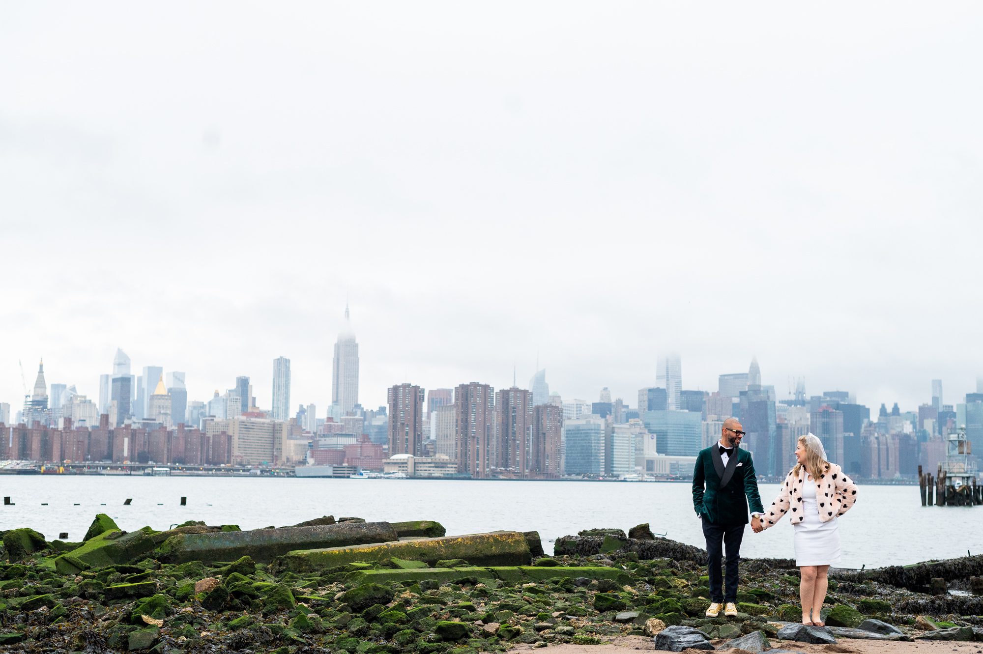 Bride and groom holding hands after eloping in Brooklyn NYC with the city skyline behind them. 