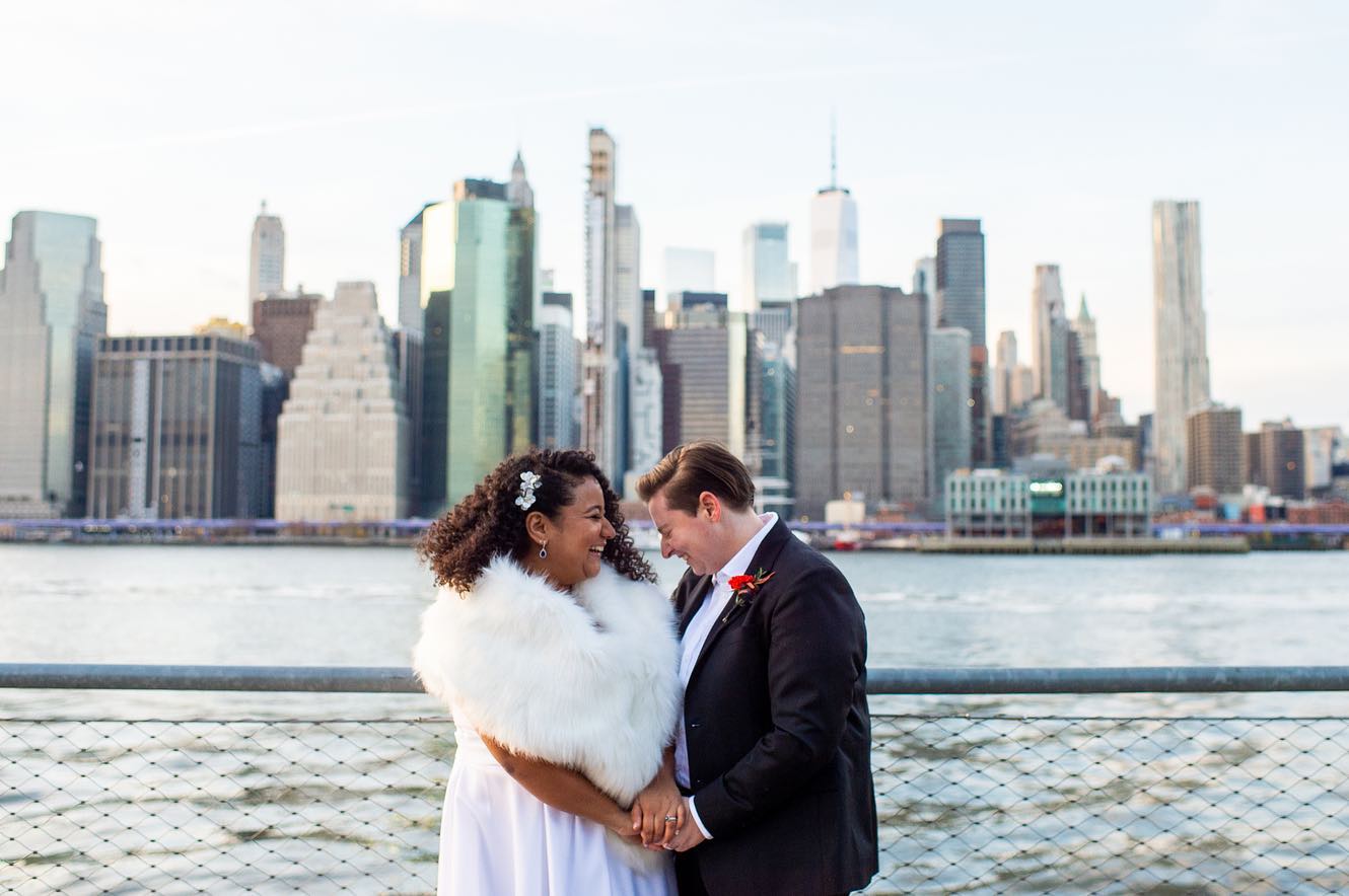 LGBTQ couple facing each other laughing after their wedding ceremony in front of the NYC Skyline 