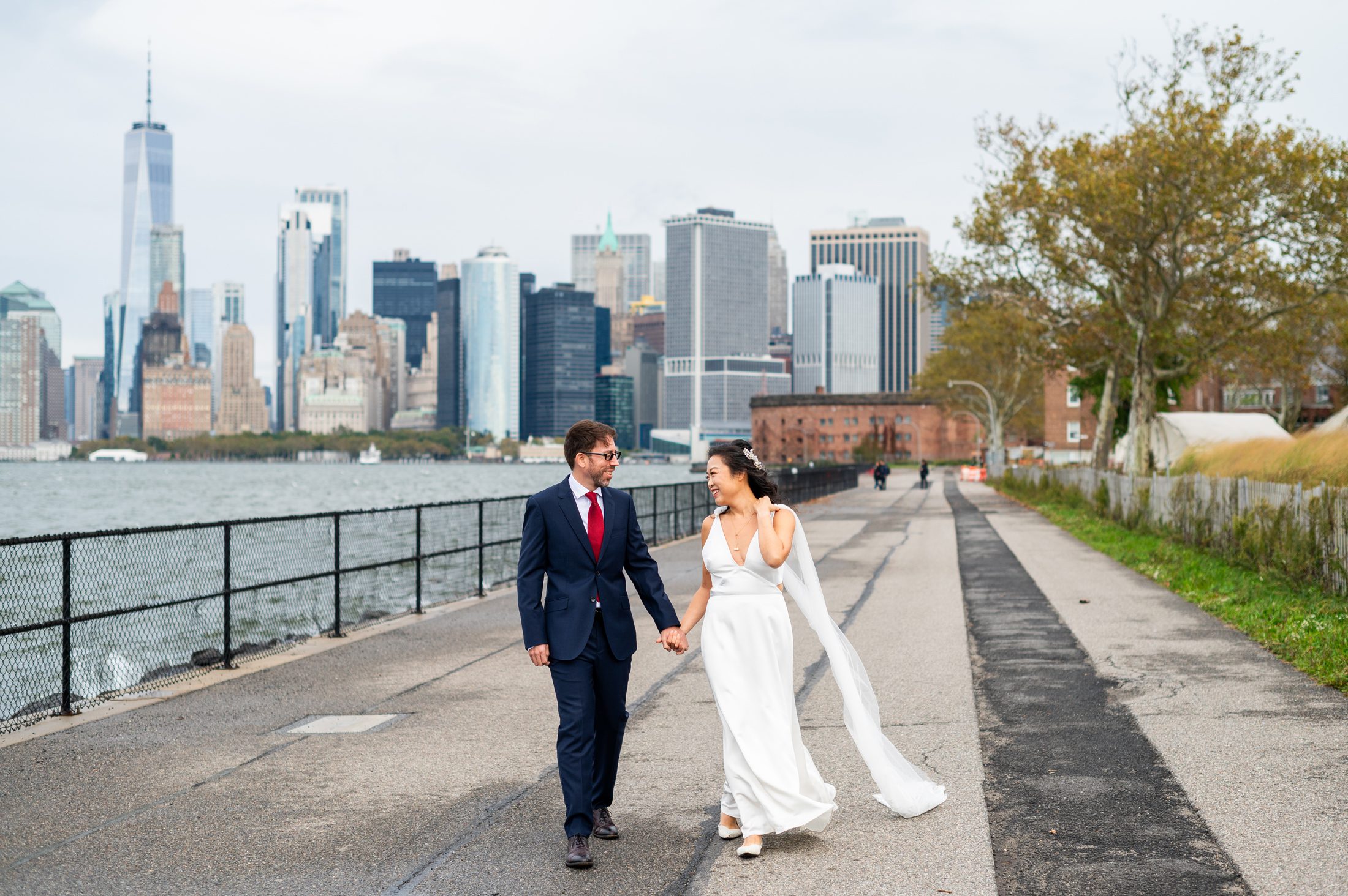 Bride and Groom walking at their wedding on Governors Island with NYC skyline in the background. 