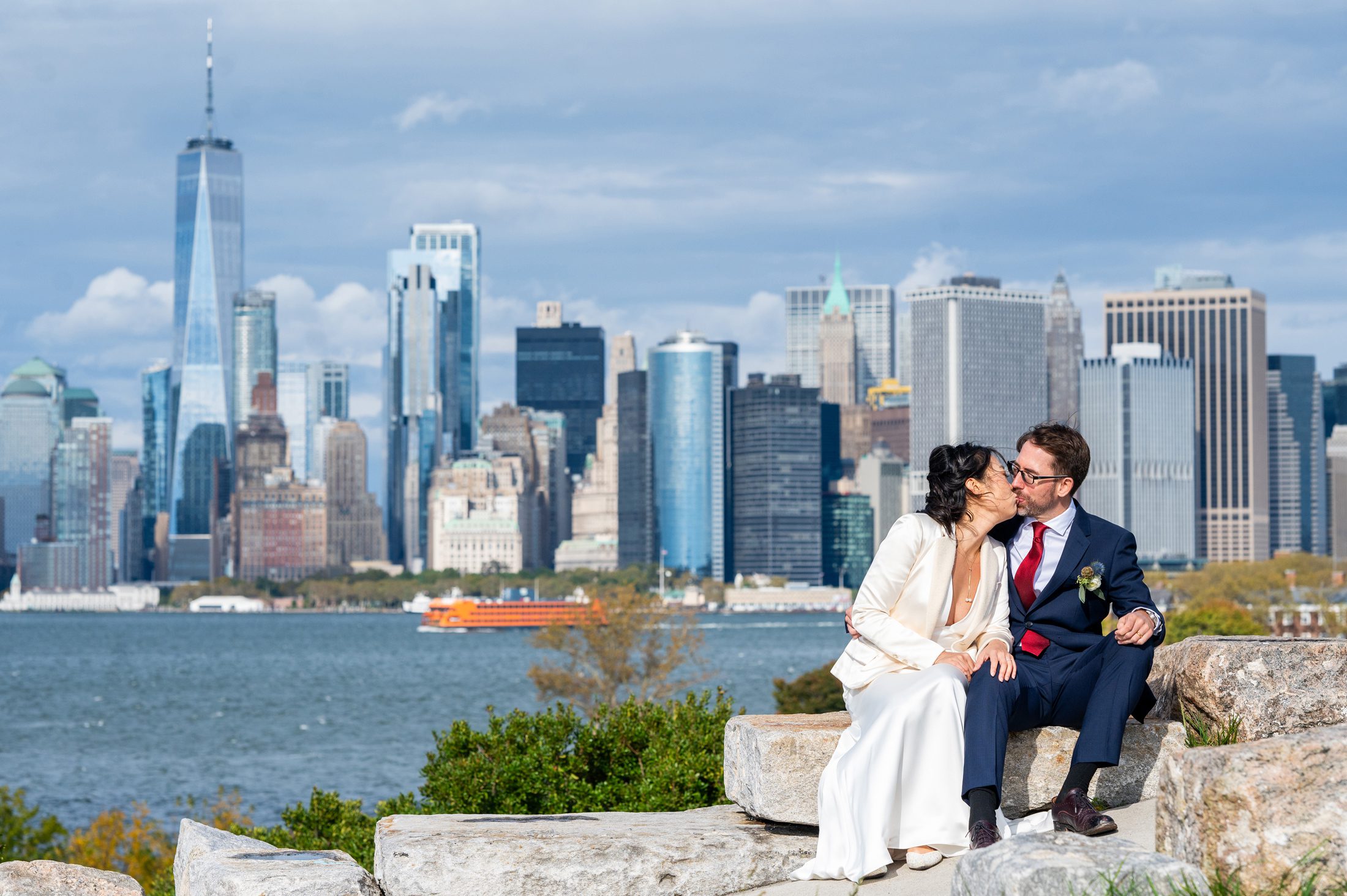 Bride and groom kissing on a rock above Governors Island in NYC. 