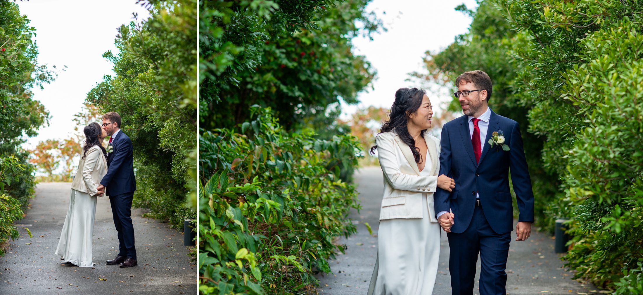 Bride and groom walking on a path with tall green bushes. 