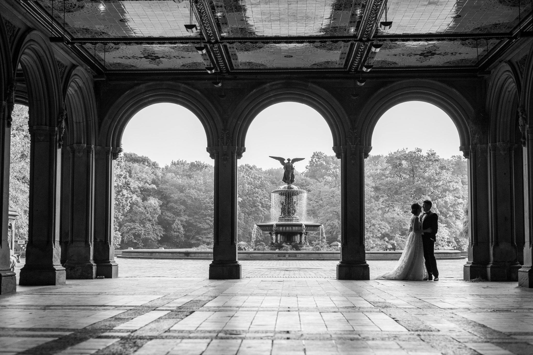Black and white photo of bride and groom under the arches of Bethesda Terrace facing the Bethesda Fountain