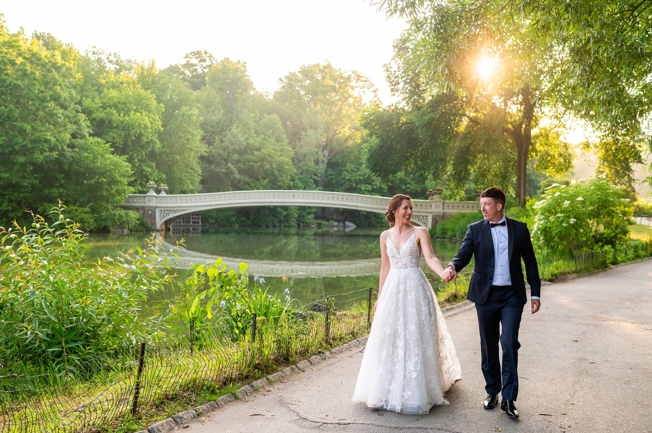 Couple walking in Central Park with Bow Bridge in the background after their sunrise wedding ceremony. 