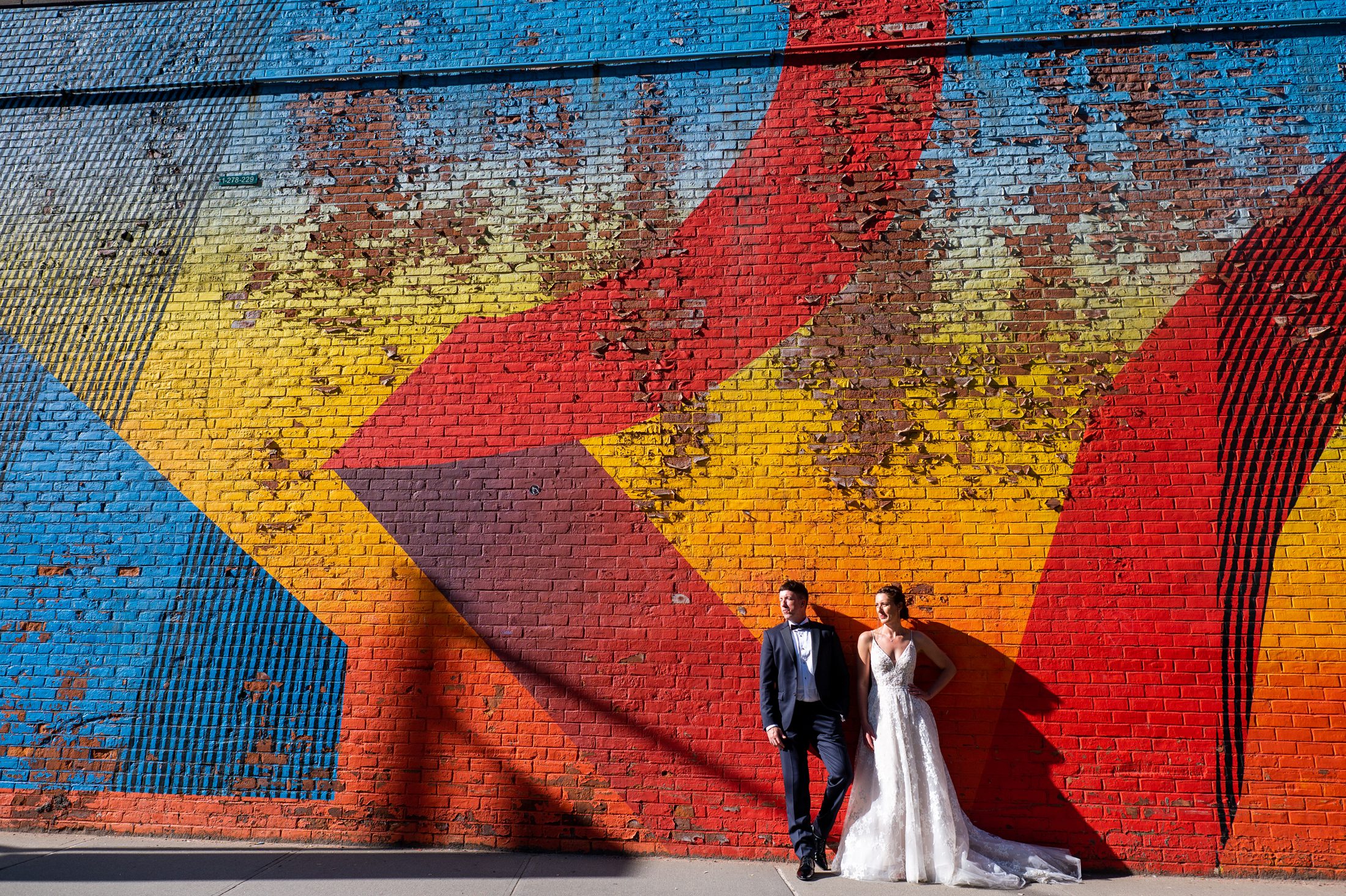 Bride and groom standing in front of colorful mural in Dumbo Brooklyn. 