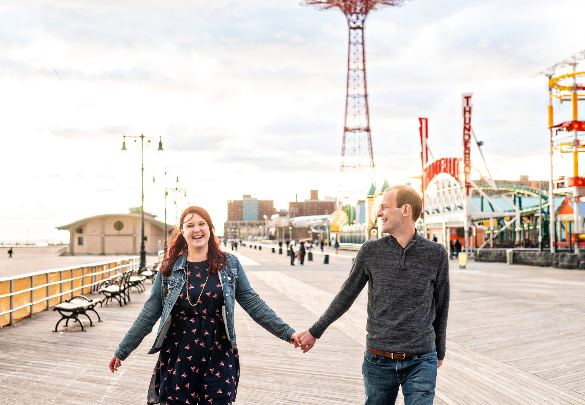 Couple walking on the boardwalk at sunset for engagement photos in Coney Island 