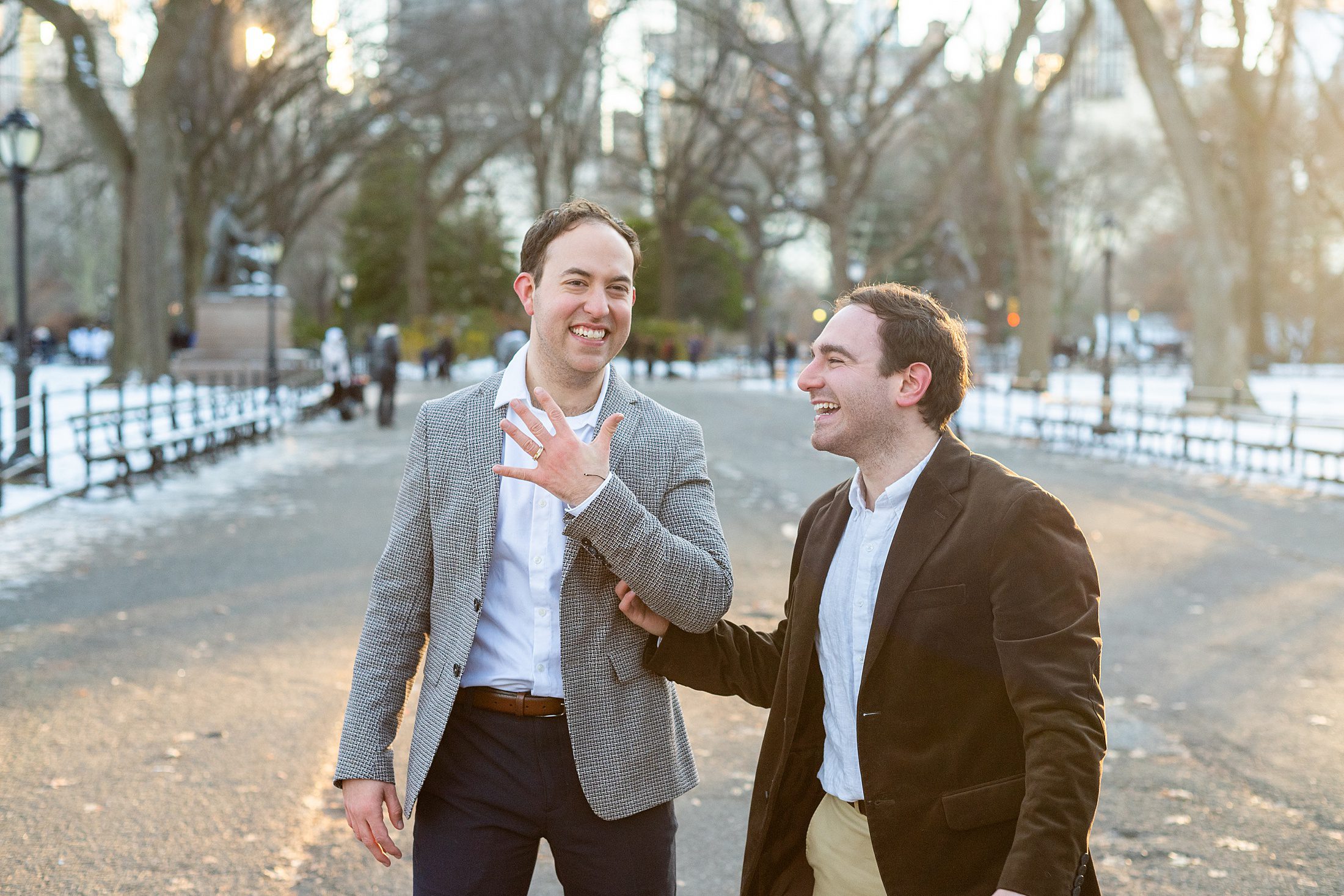 LGBT couple showing off rings, excited about getting engaged in Central Park at sunset