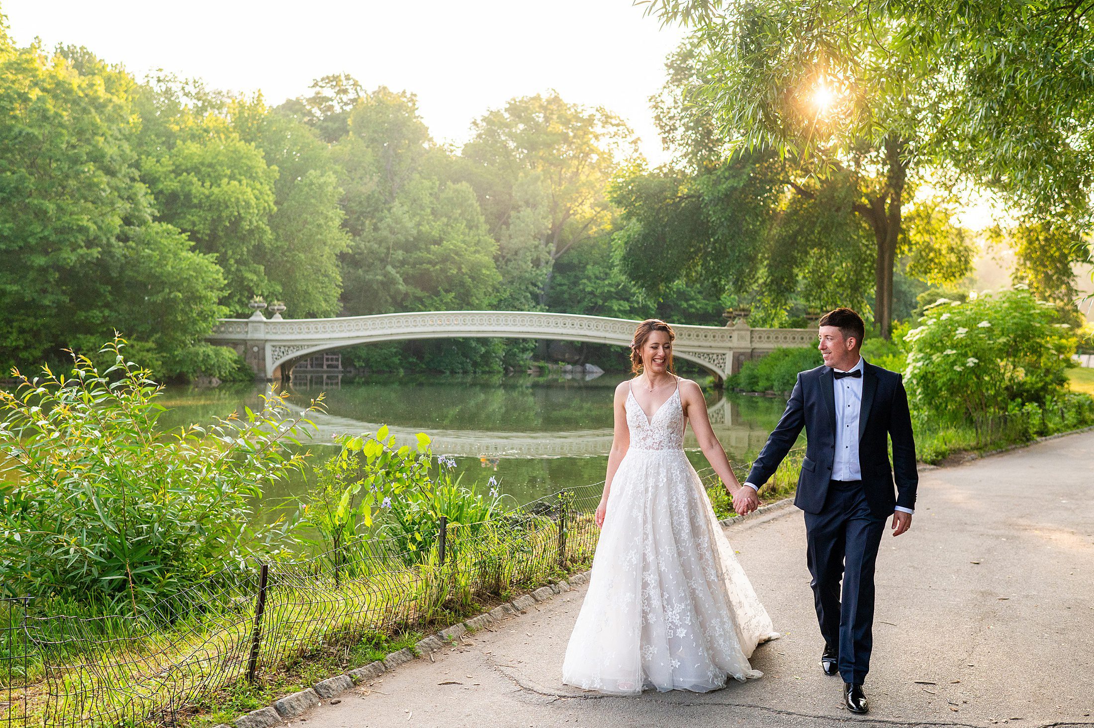 Sunrise summer elopement in NYC with bride and groom walking past bow bridge in Central Park